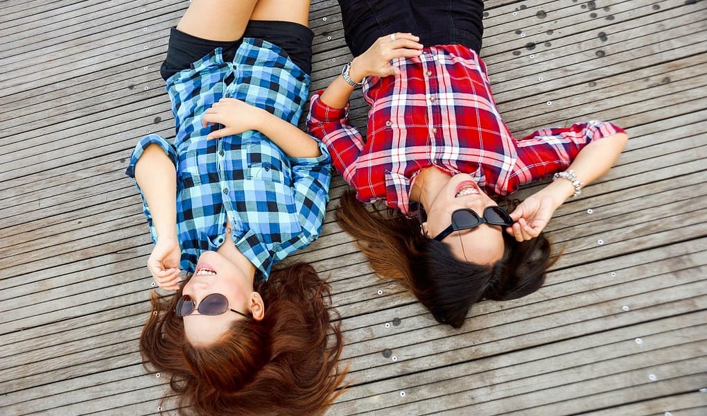 two woman wearing blue and red sport shirts and sunglasses lying on brown surface