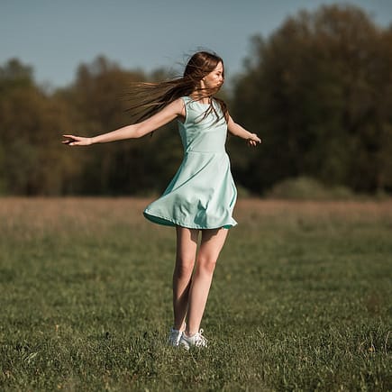 positive young woman dancing in meadow on sunny day