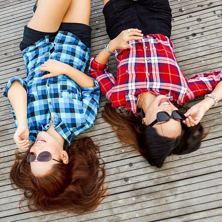 two woman wearing blue and red sport shirts and sunglasses lying on brown surface
