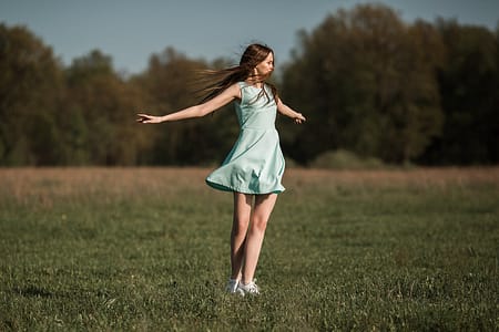 positive young woman dancing in meadow on sunny day